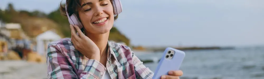 Woman sitting next to the ocean, holding a mobile phone