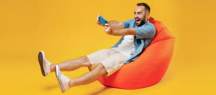 man sitting on a pillow chair celebrating a win on a game on a mobile device 